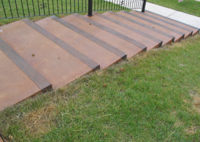 A sidewalk with steps and grass next to a fence.