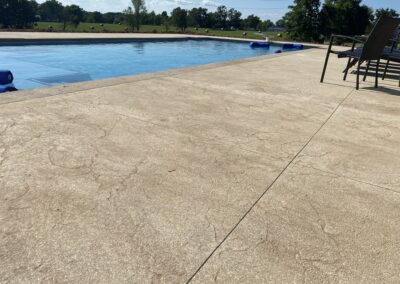 A concrete patio with a pool in the background.